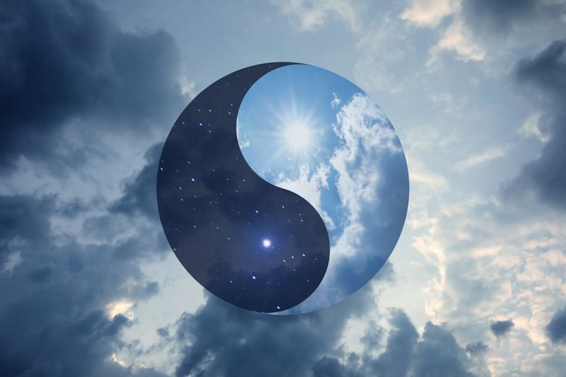 Símbolo de Yin y Yang proyectado sobre un cielo azul con nubes y sol en el centro