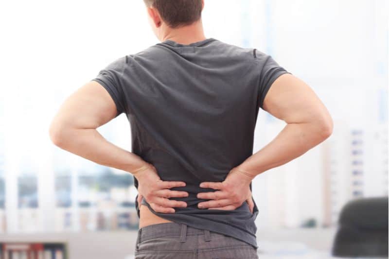 El dolor lumbar puede aliviarse con los puntos de acupuntura para lumbalgia. Se muestra a un hombre de espaldas tocándose la zona lumbar
