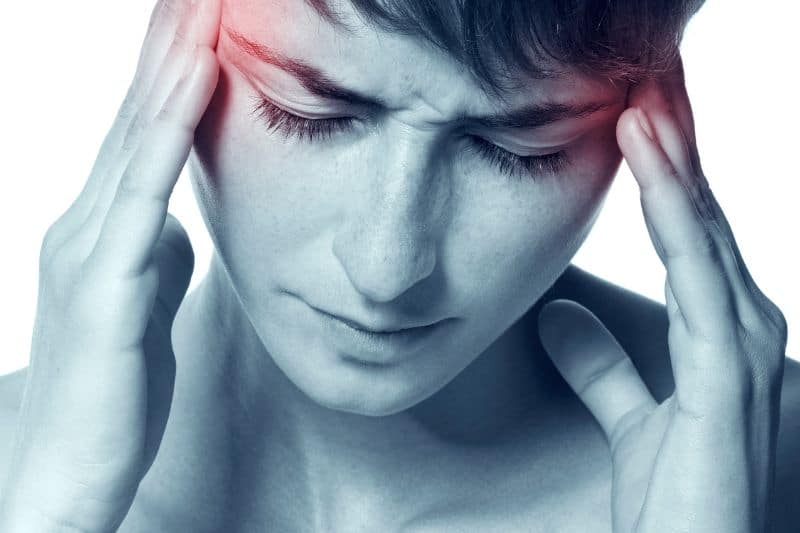 El dolor de la migraña se aprecia especialmente en la sien, zona temporal, pero también en la frente, occipital, cuello y hombros. La foto muestra a una mujer con un tono azulado, con sus manos sobre las sienes que aparecen enrojecidas